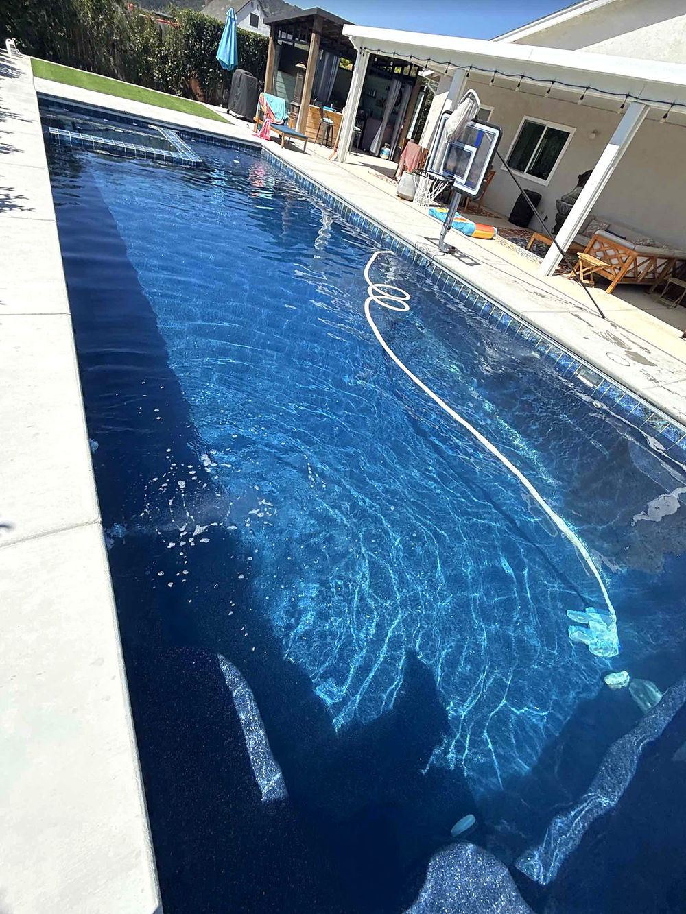 Full length of a forty-foot Latham Astoria 16 fiberglass pool alongside a covered patio
