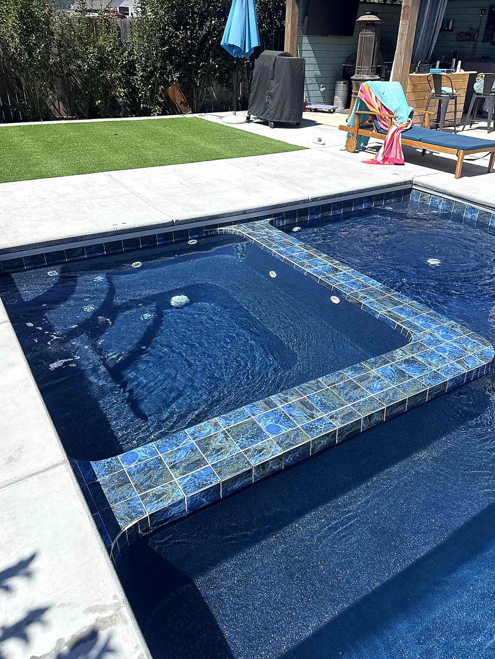 Spa and tanning ledge of a completed Latham Astoria 16 with turf lawn and covered patio