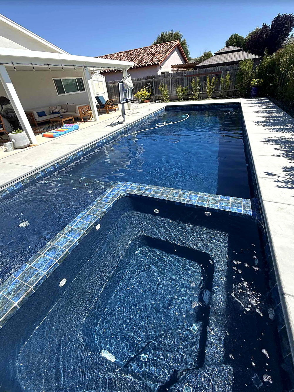 Integrated spa spilling over a glass-tile dam wall into the main pool of a completed Latham Astoria 16
